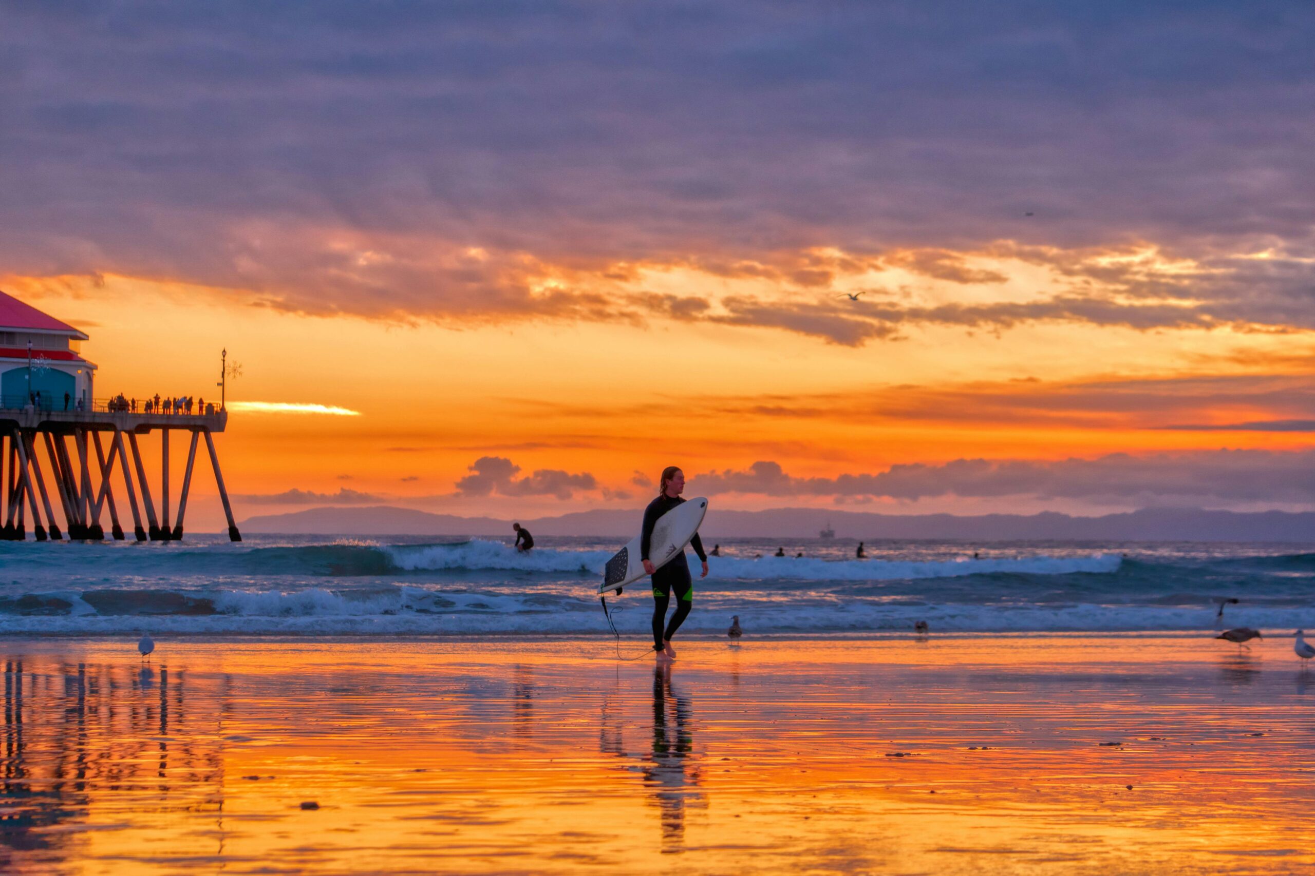 Orange County beach at sunset with a surfer and the pier in the background symbolizing peace and serenity during medical detox at Ocean Hills Recovery in Dana Point, California.